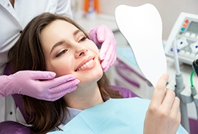 woman smiling while looking in dental mirror 