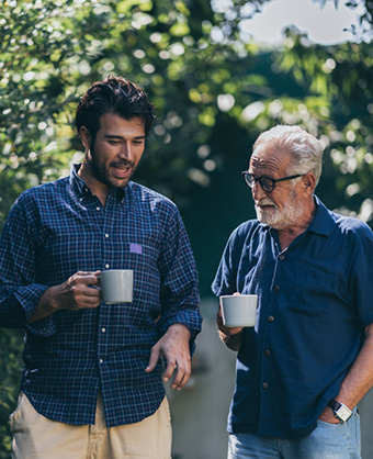 Two men holding coffee mugs and talking outdoors