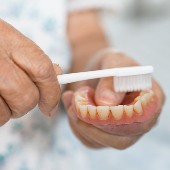 Person cleaning a denture with a toothbrush