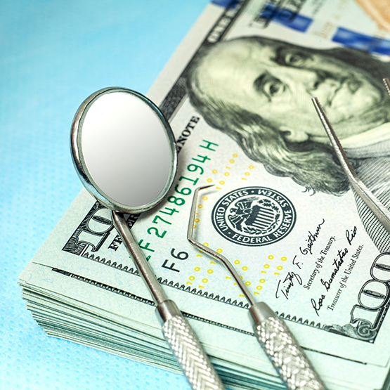 Dental instruments resting on a stack of dollar bills