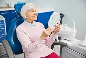 Senior woman in dental chair checking smile in mirror
