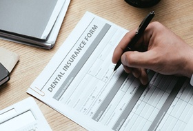 Close-up of man’s hand filling out dental insurance form