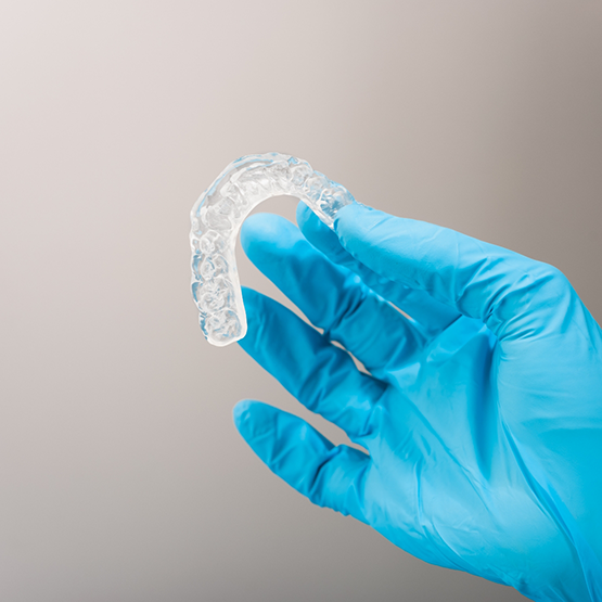 Gloved hand holding a clear nightguard