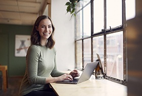 smiling person sitting in a coffee shop and working on their laptop