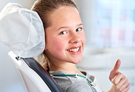 Little girl in dental chair giving thumbs up