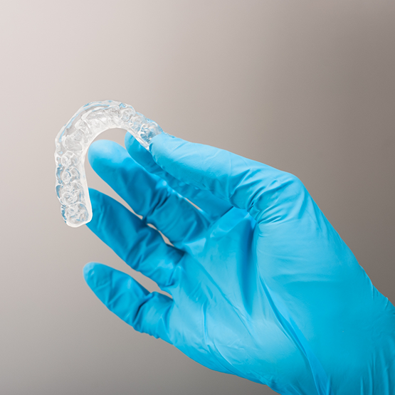 Gloved hand holding a clear nightguard