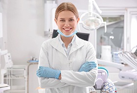 A female dentist wearing gloves, a lab coat, and a mask in preparation to see a new patient
