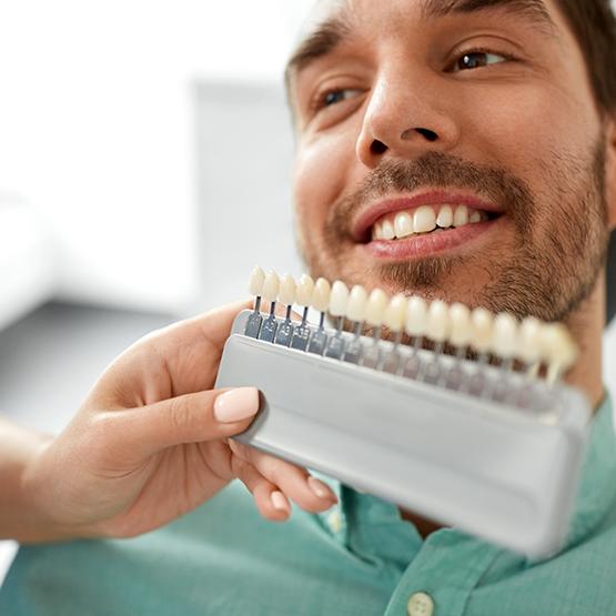 Dentist holding a shade guide in front of a patient's teeth