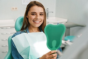 Woman sitting in dental chair smiling and looking at handheld mirror