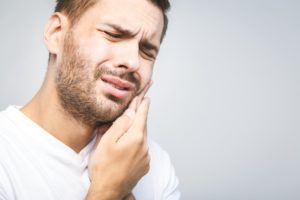 a young man holding his cheek in pain and in need of an emergency dentist in Corbin