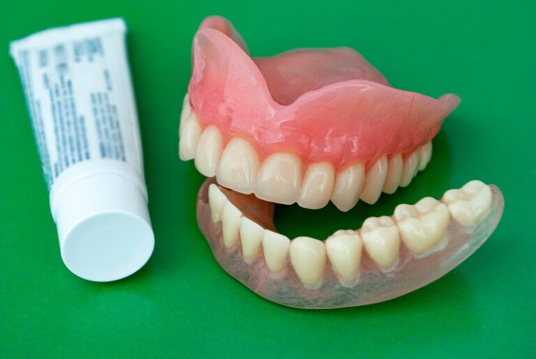 A tube of denture adhesive next to prosthetic teeth