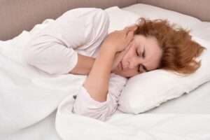 Woman lying in bed, suffering from a toothache 